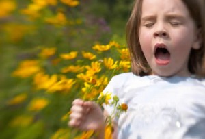 girl sneezing into flowers because of pollen allergy